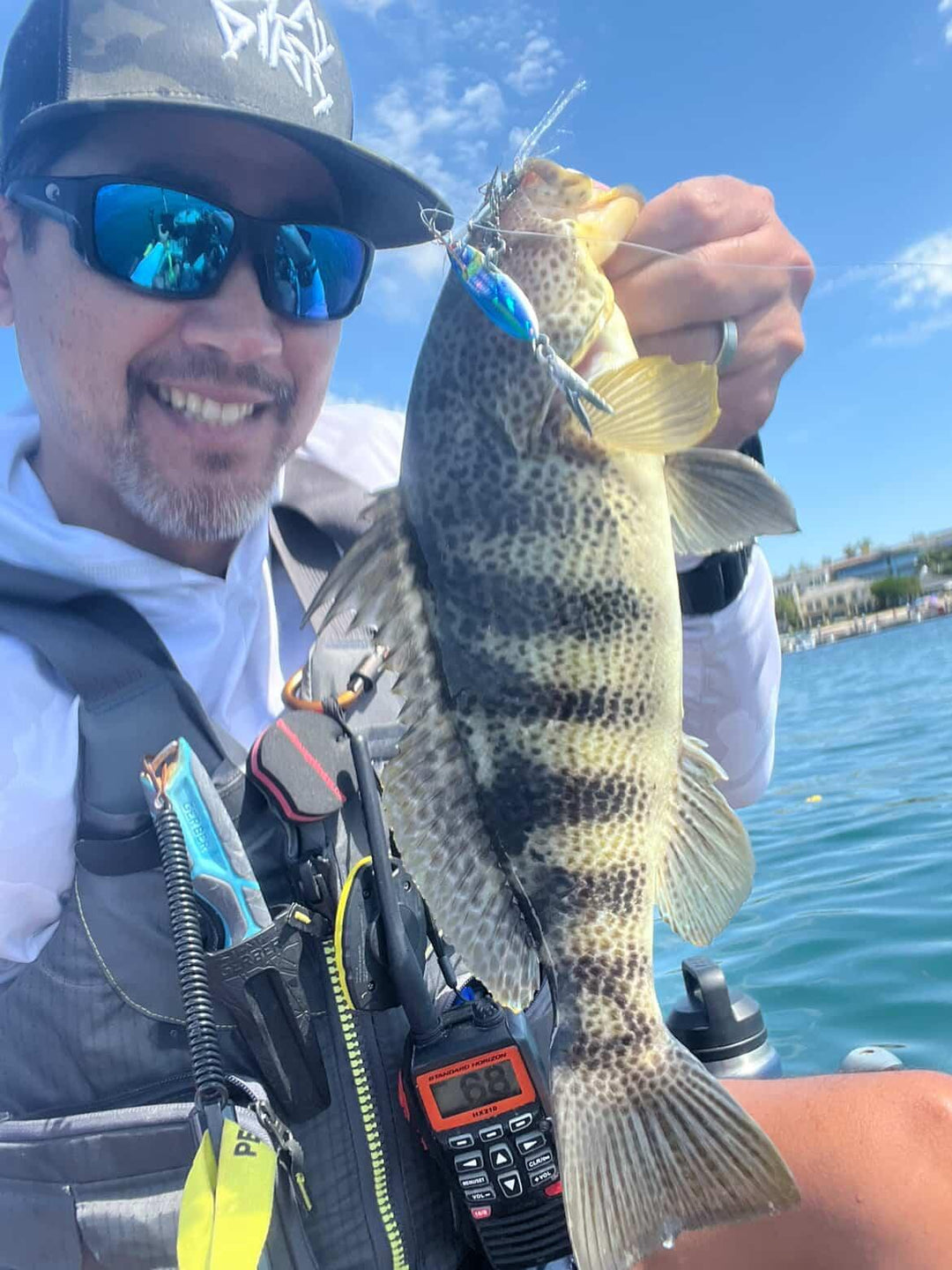 Angler holding a spotted bay bass caught on a Submission Fishing slow pitch jig during an inshore saltwater fishing trip.