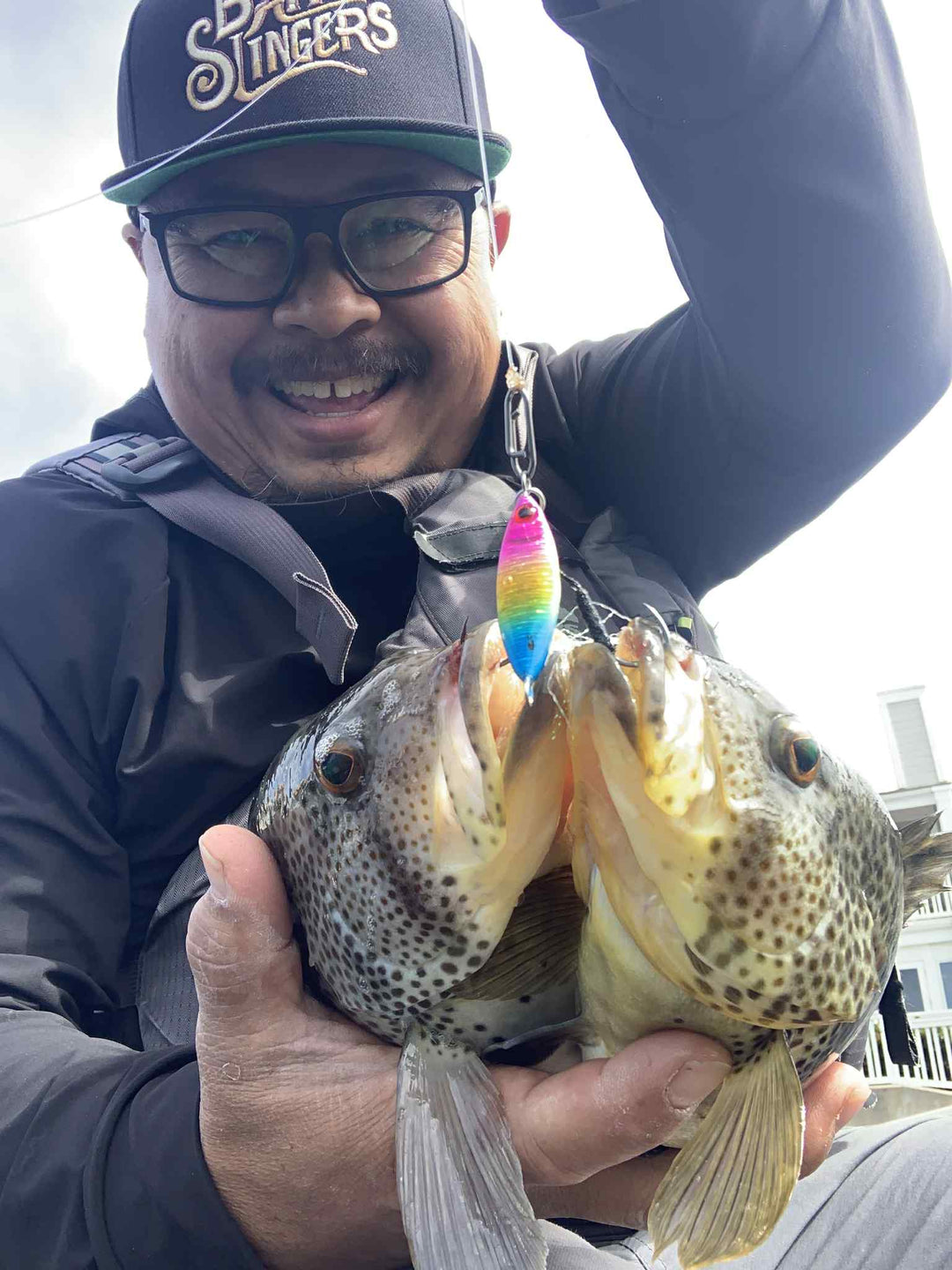 Angler holding two spotted bay bass caught on a Submission Fishing Sumo Rainbow micro slow pitch jig.